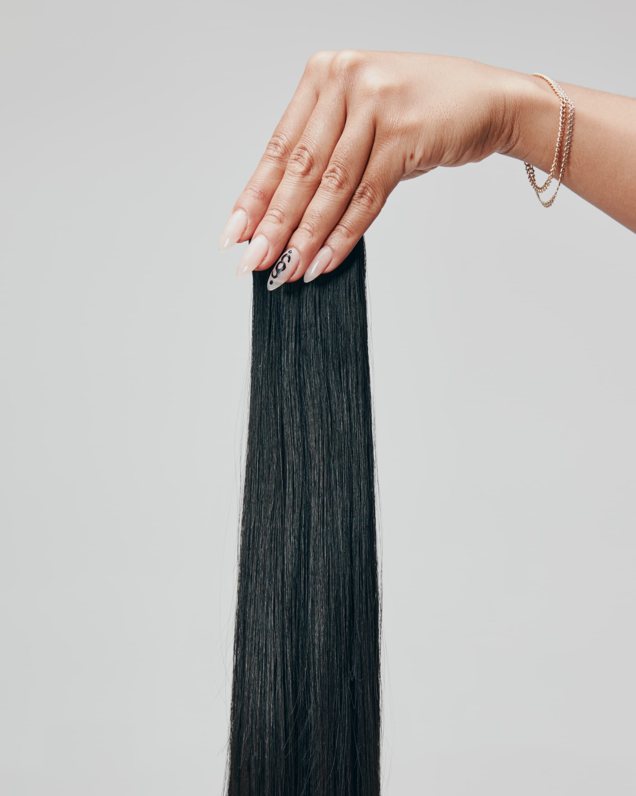 Hand holding a black hair extension against a gray background