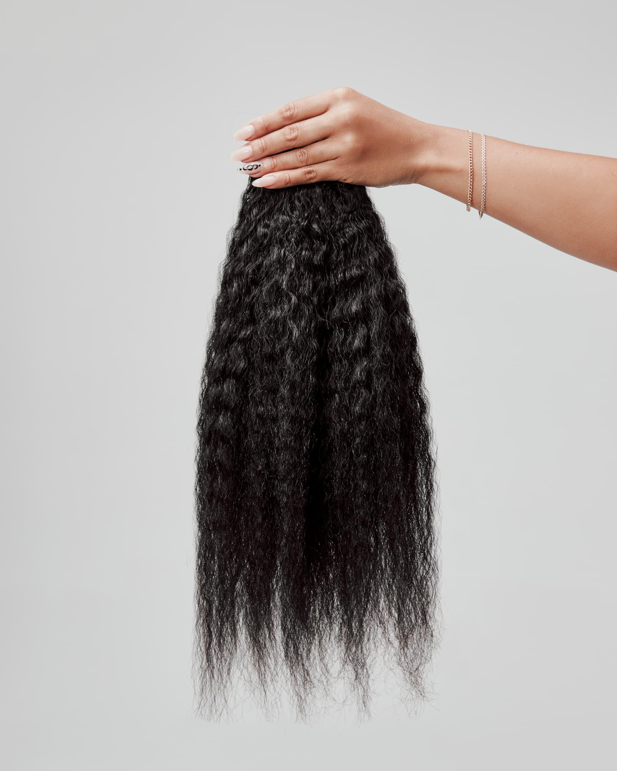 Black hair extensions held by a hand on a light gray background