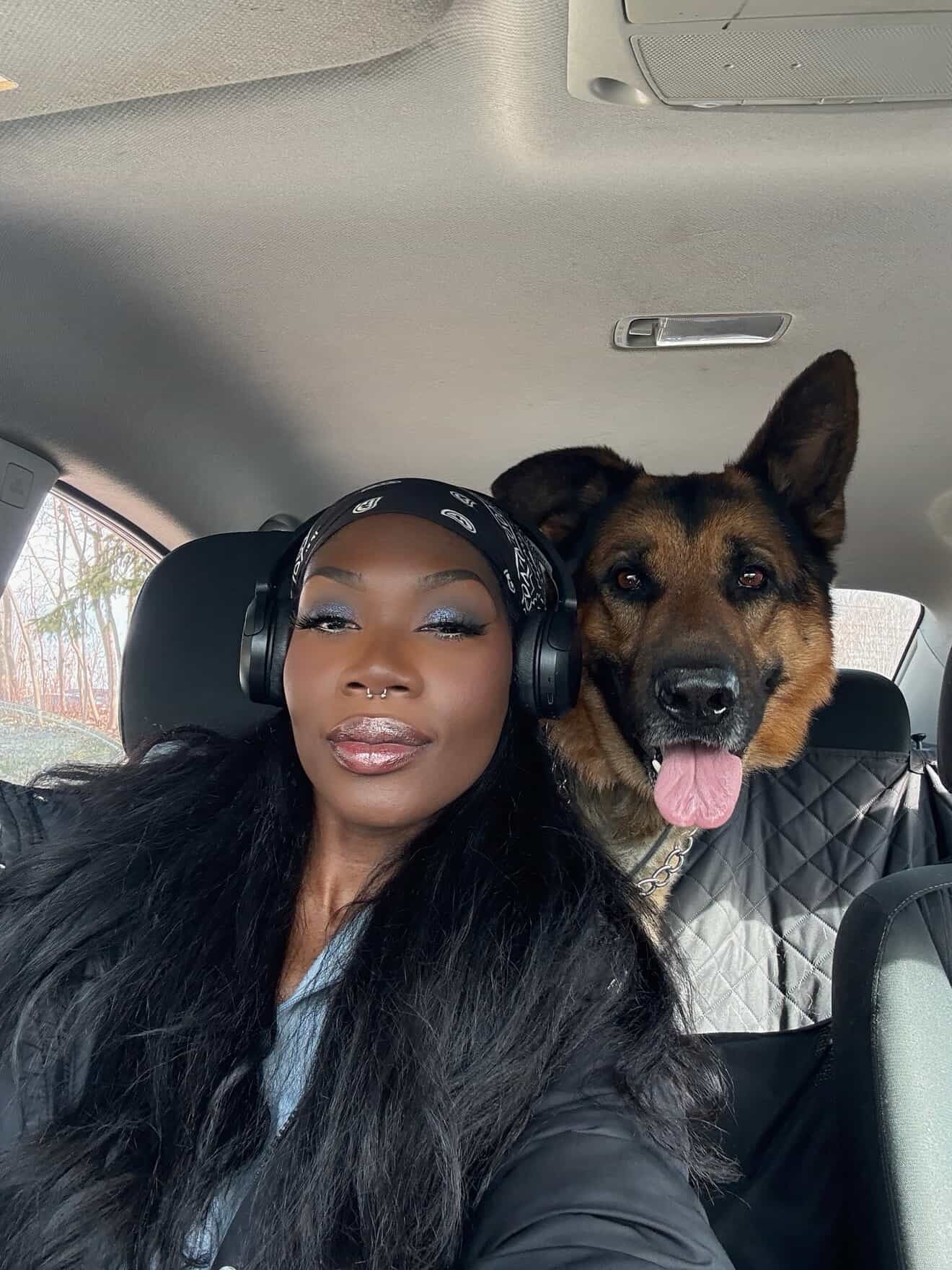 Woman wearing headphones sitting in a car with a German Shepherd dog.