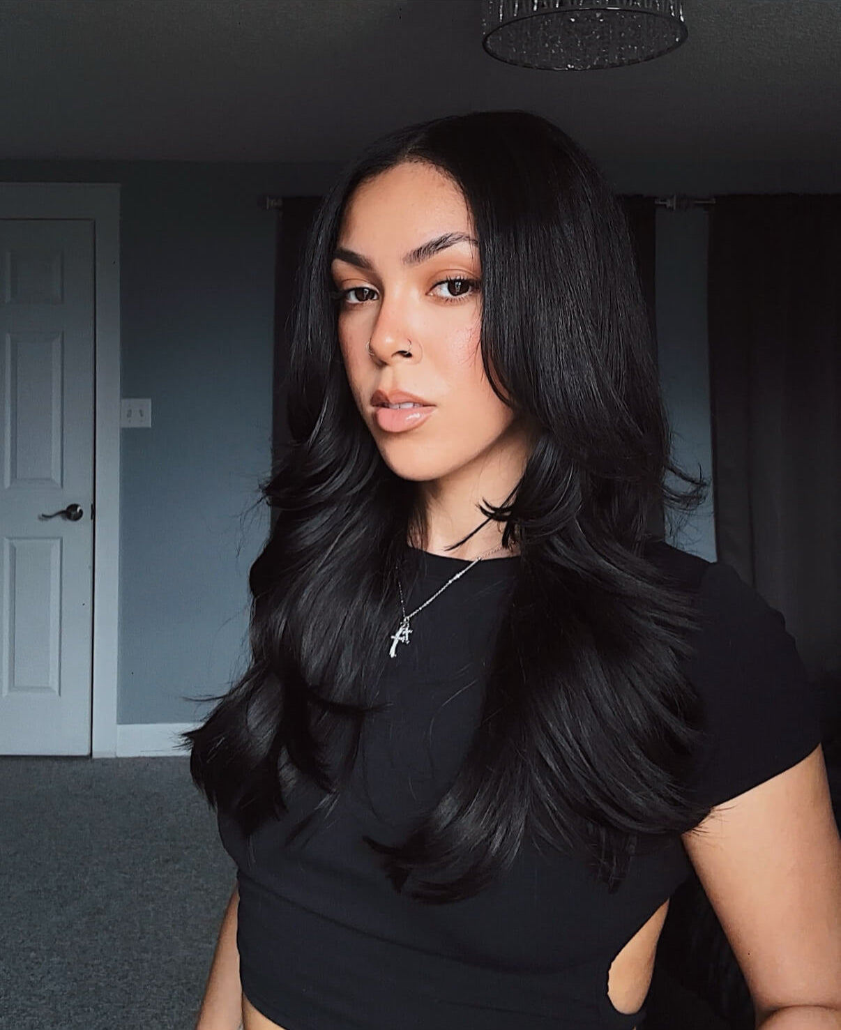 Woman with long black hair extensions wearing a black top in an indoor setting.
