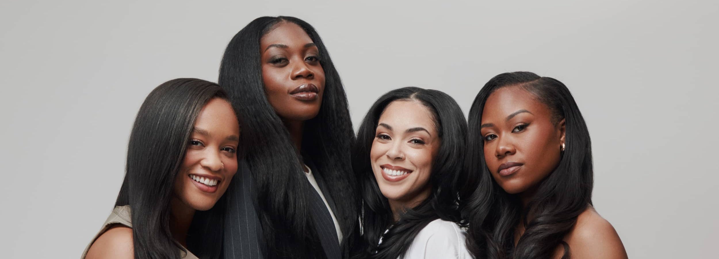 Four women with long, straight hair posing together against a plain background