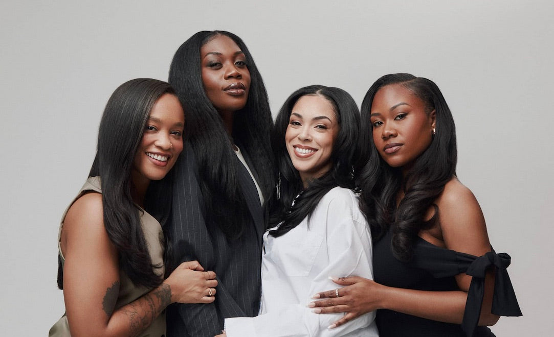 Four women with styled hair posing together against a neutral background