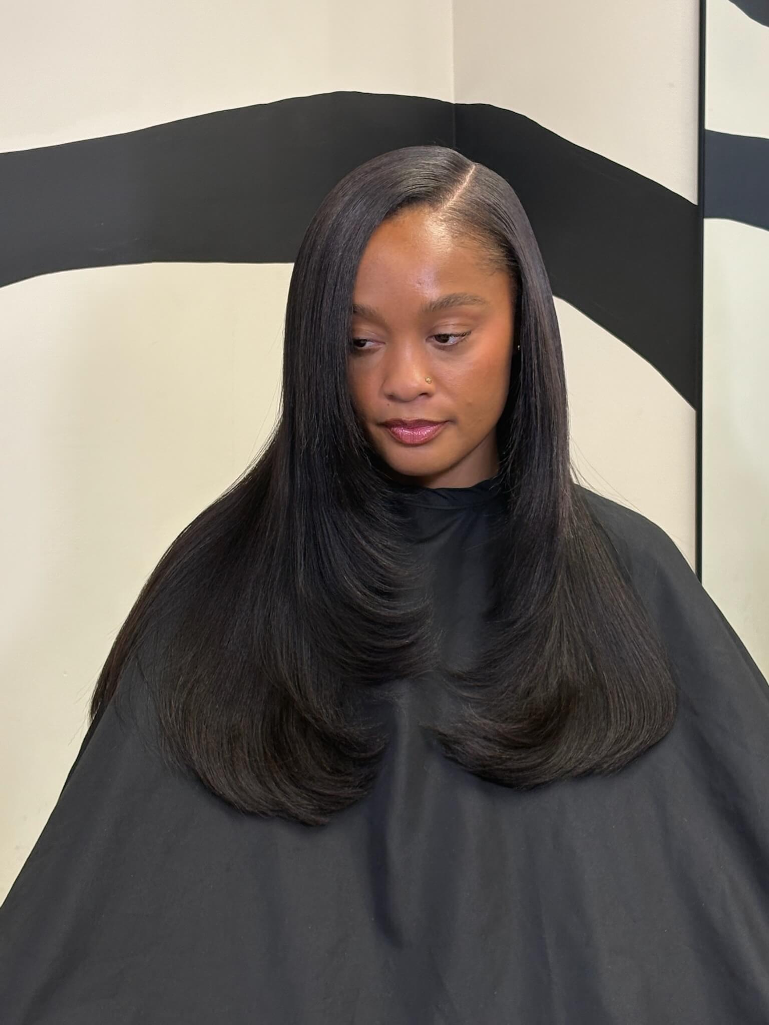 Woman with long black hair sitting in a salon chair.